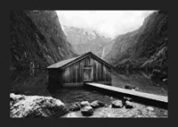 Black and white photo of wooden cabin by lake, surrounded by high mountains-5