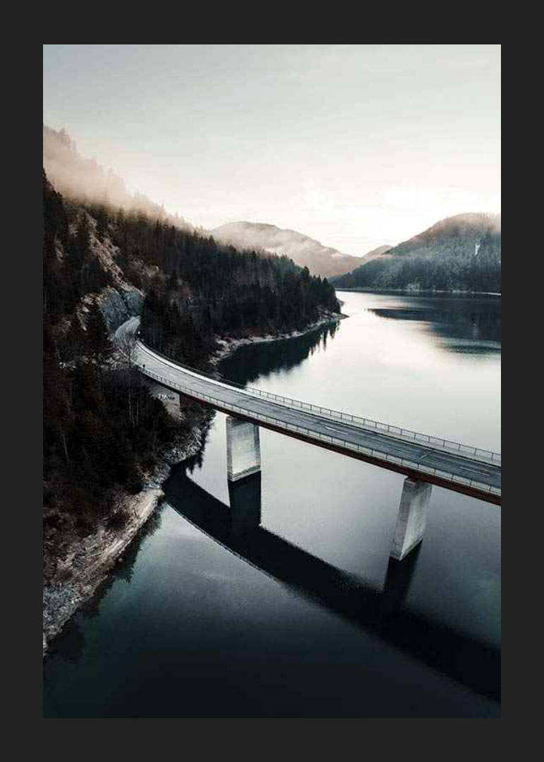 Photographic bridge over calm lake with forested mountains-12