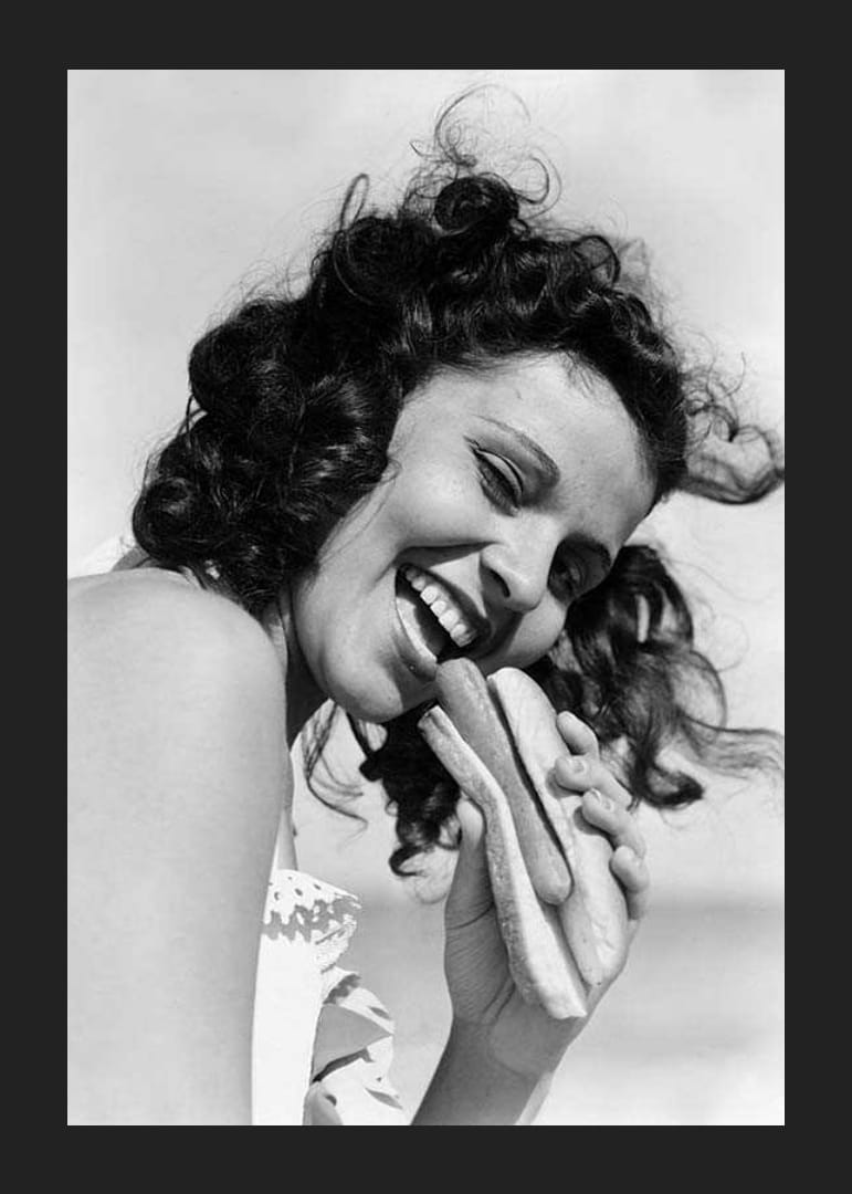 Photographie en noir et blanc d'une femme souriante avec un hot-dog à l'extérieur-12