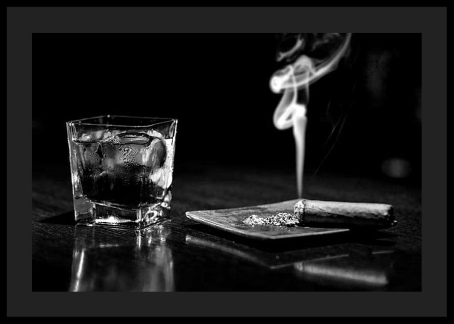 Mustavalkoinen valokuva viskilasista ja tupakoivasta sikarista pöydällä-12