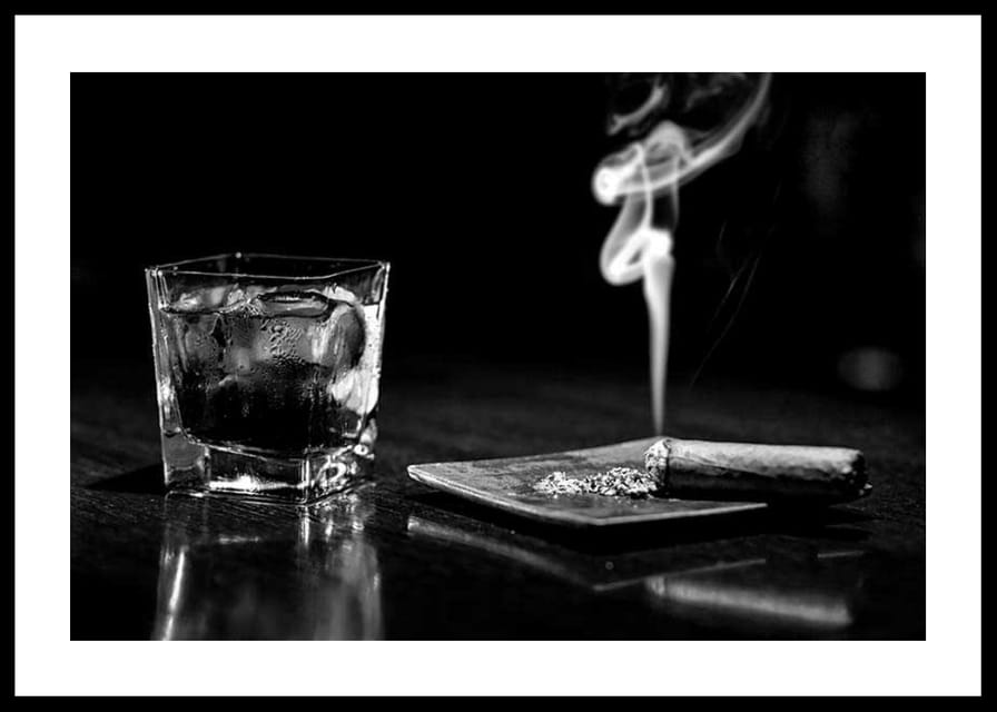 Mustavalkoinen valokuva viskilasista ja tupakoivasta sikarista pöydällä-12