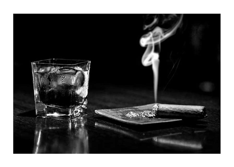 Mustavalkoinen valokuva viskilasista ja tupakoivasta sikarista pöydällä-12