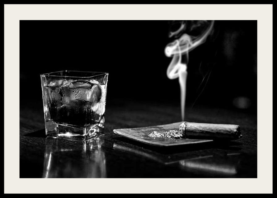 Mustavalkoinen valokuva viskilasista ja tupakoivasta sikarista pöydällä-12