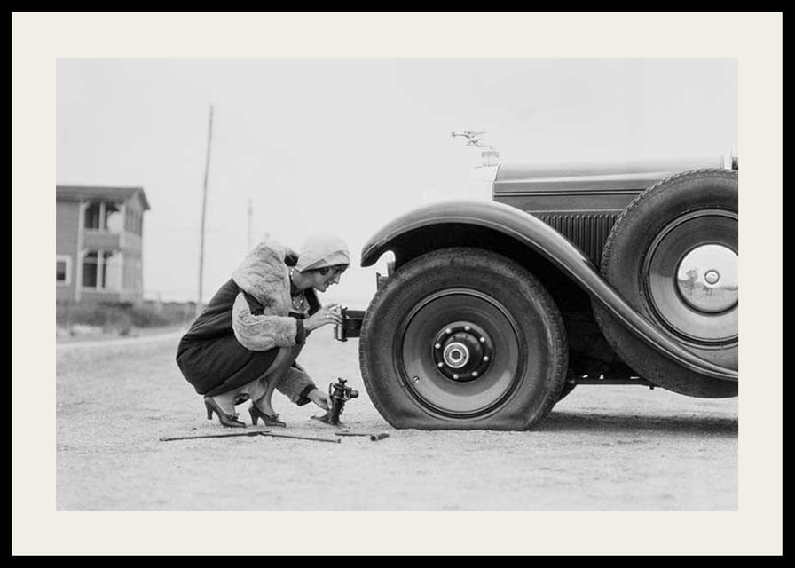 Fotografía en blanco y negro de una mujer cambiando un neumático de un coche clásico.-12