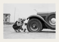 Fotografía en blanco y negro de una mujer cambiando un neumático de un coche clásico.-3