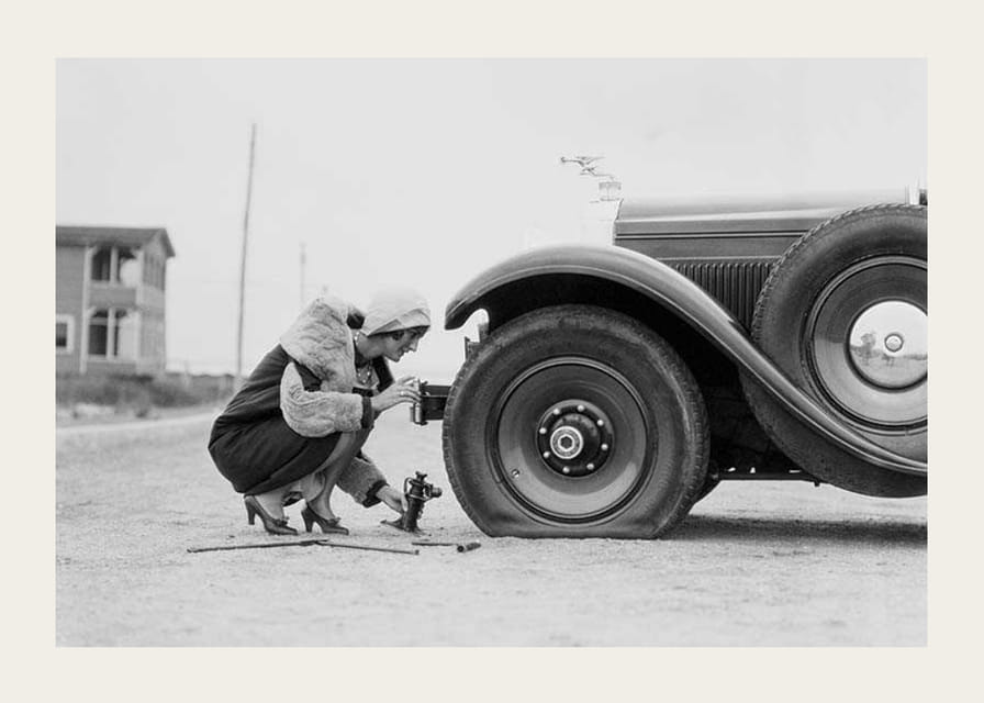 Fotografía en blanco y negro de una mujer cambiando un neumático de un coche clásico.-12