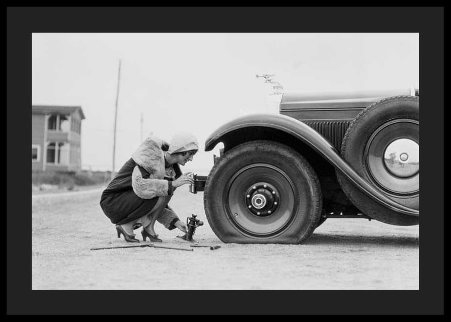 Fotografía en blanco y negro de una mujer cambiando un neumático de un coche clásico.-12