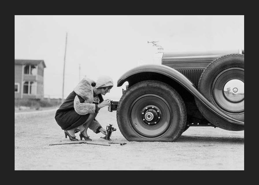 Fotografía en blanco y negro de una mujer cambiando un neumático de un coche clásico.-12