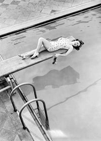 Black and white photograph of woman on trampoline above pool-7