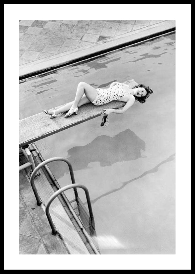Black and white photograph of woman on trampoline above pool-12