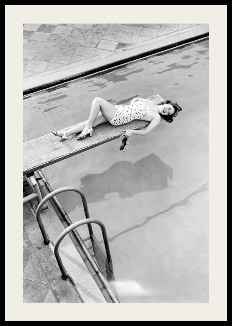 Black and white photograph of woman on trampoline above pool-12