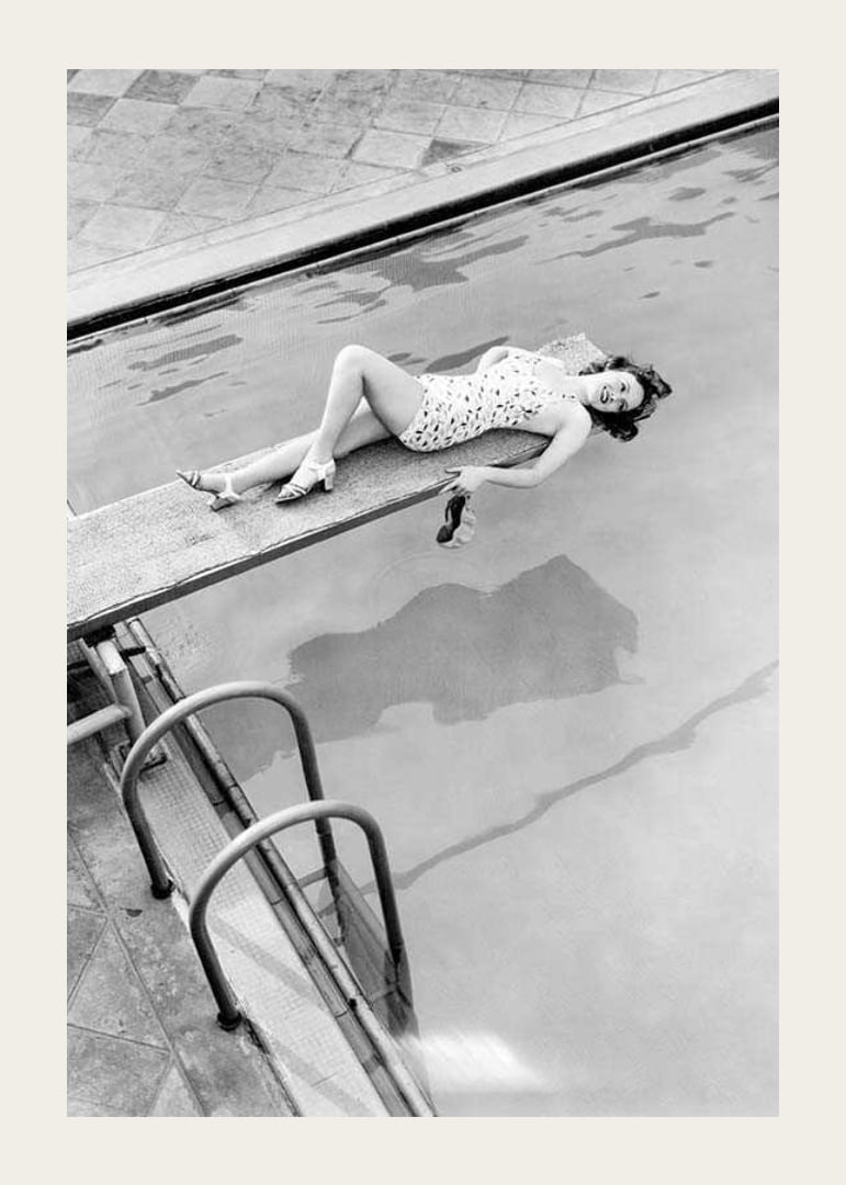 Black and white photograph of woman on trampoline above pool-12