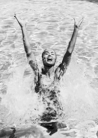 Black and white photo of smiling woman splashing water in pool-7