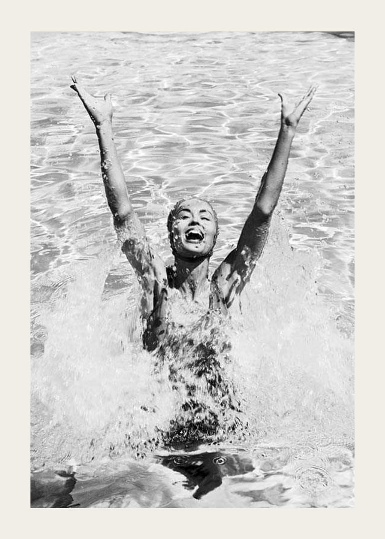 Schwarz-Weiß-Foto einer lächelnden Frau, die im Pool Wasser planscht-12