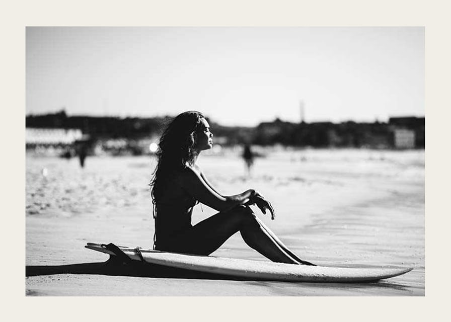 Black and white photo of woman on surfboard at sandy beach-12