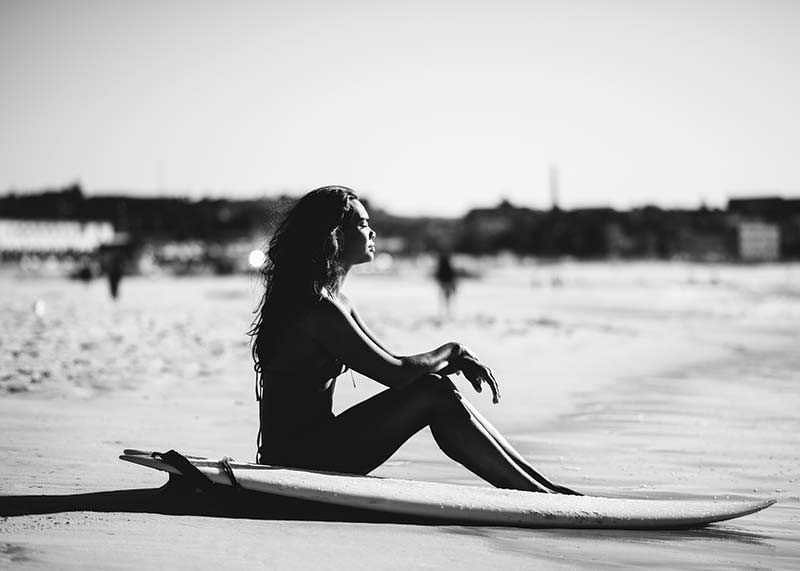 Black and white photo of woman on surfboard at sandy beach-12