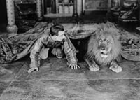 Black and white photograph of young man and lion on floor indoors-7