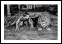 Black and white photograph of young man and lion on floor indoors-0