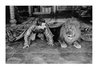 Black and white photograph of young man and lion on floor indoors-1