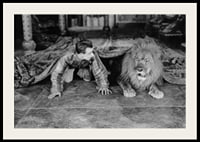 Black and white photograph of young man and lion on floor indoors-2