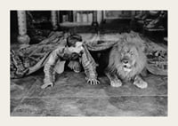 Black and white photograph of young man and lion on floor indoors-3