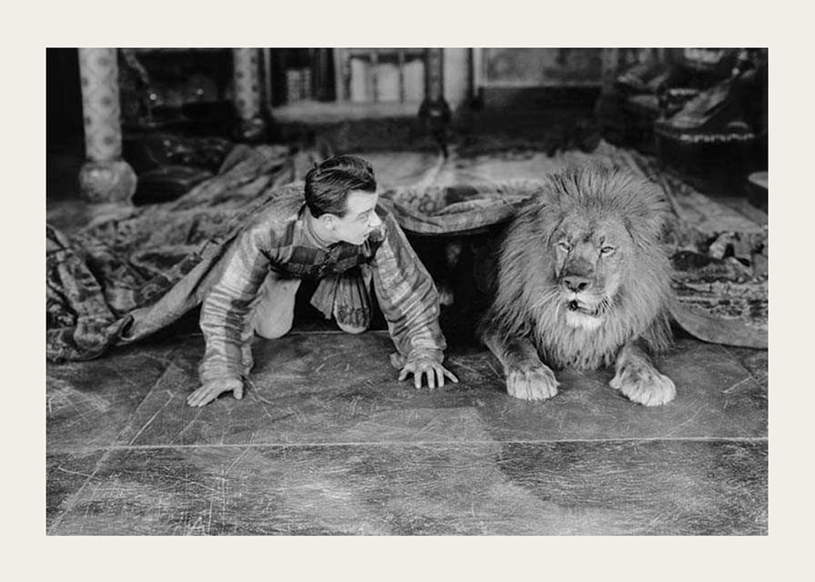 Black and white photograph of young man and lion on floor indoors-12