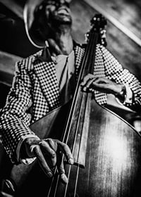 Black and white close-up of man in checkered jacket playing double bass-7
