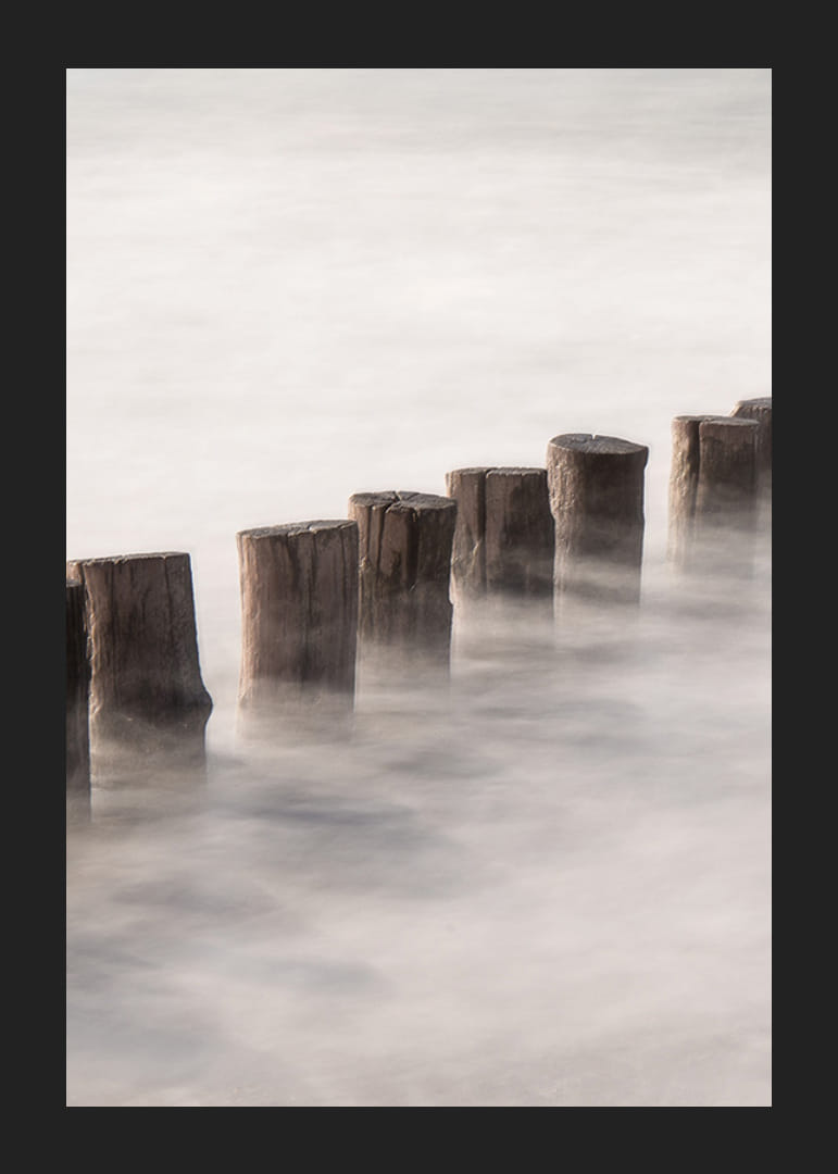 Fotografia di pali di legno in linea retta circondati dalla superficie nebbiosa del mare-12