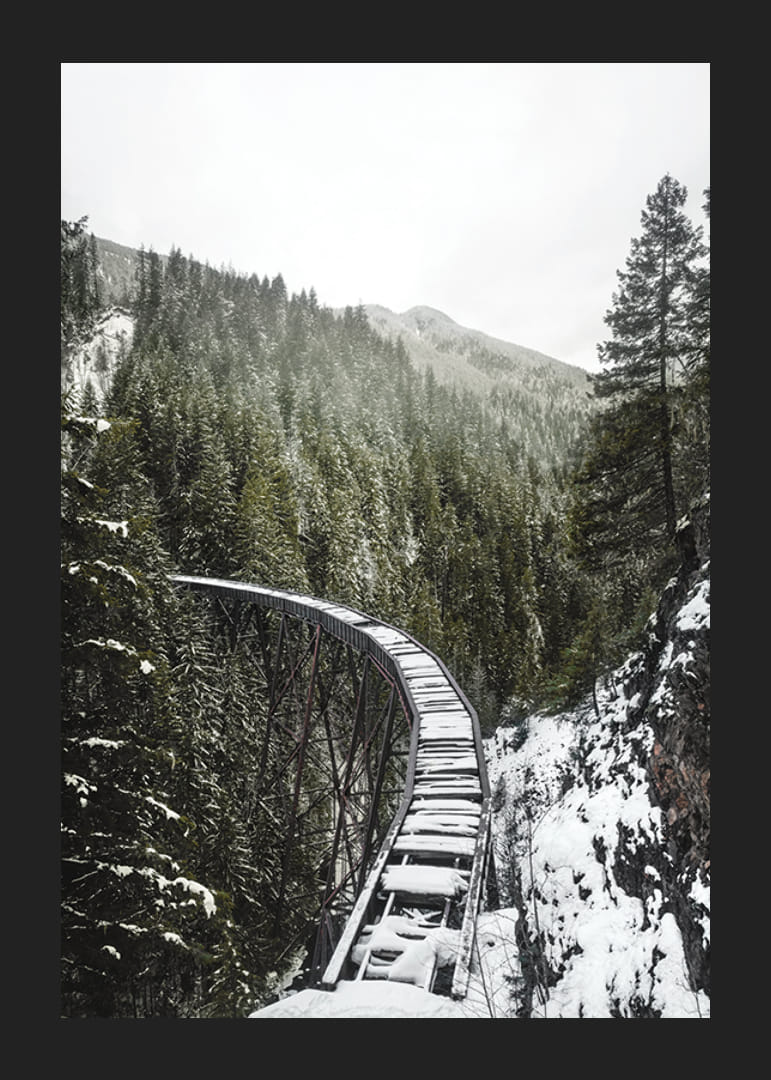 Fénykép egy hófödte vasúti hídról lucfenyőerdő felett téli tájban-12
