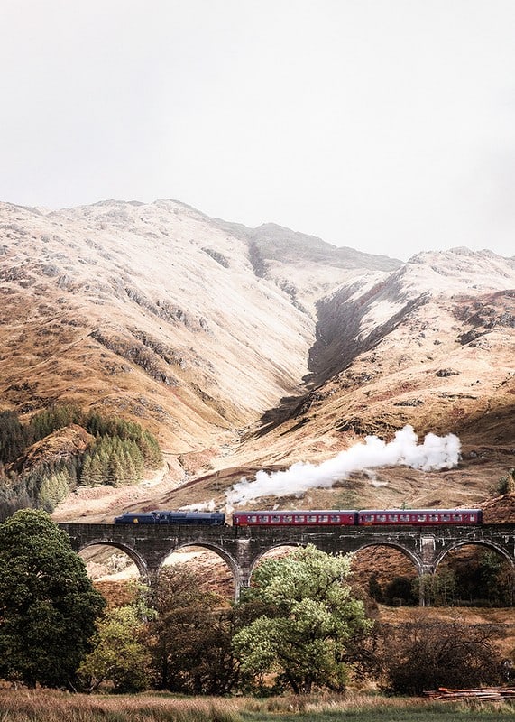 Steam train on stone viaduct in front of bright mountains in autumn landscape-12