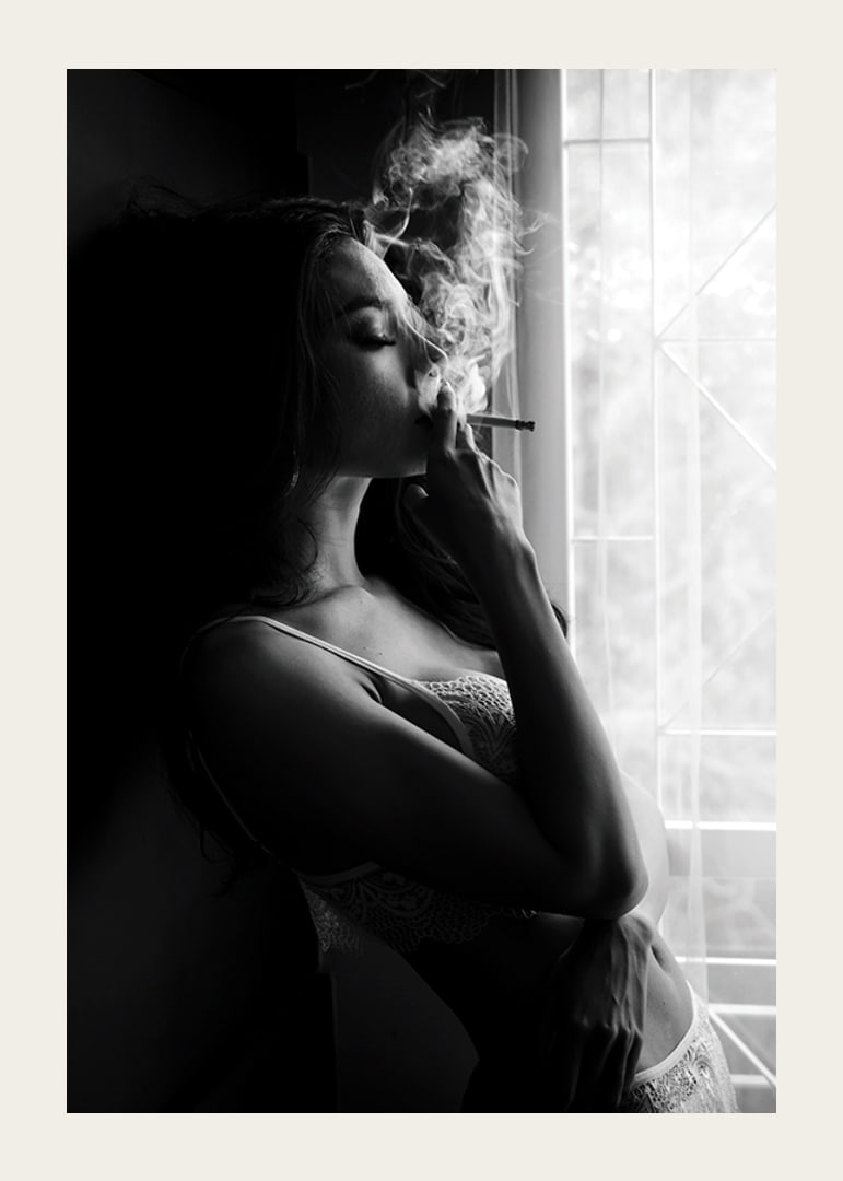 Black and white photograph of woman smoking by a window-12