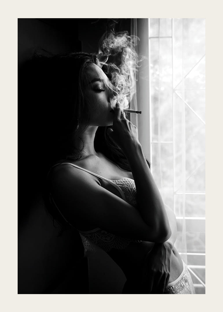 Photographie en noir et blanc d'une femme fumant près d'une fenêtre-12