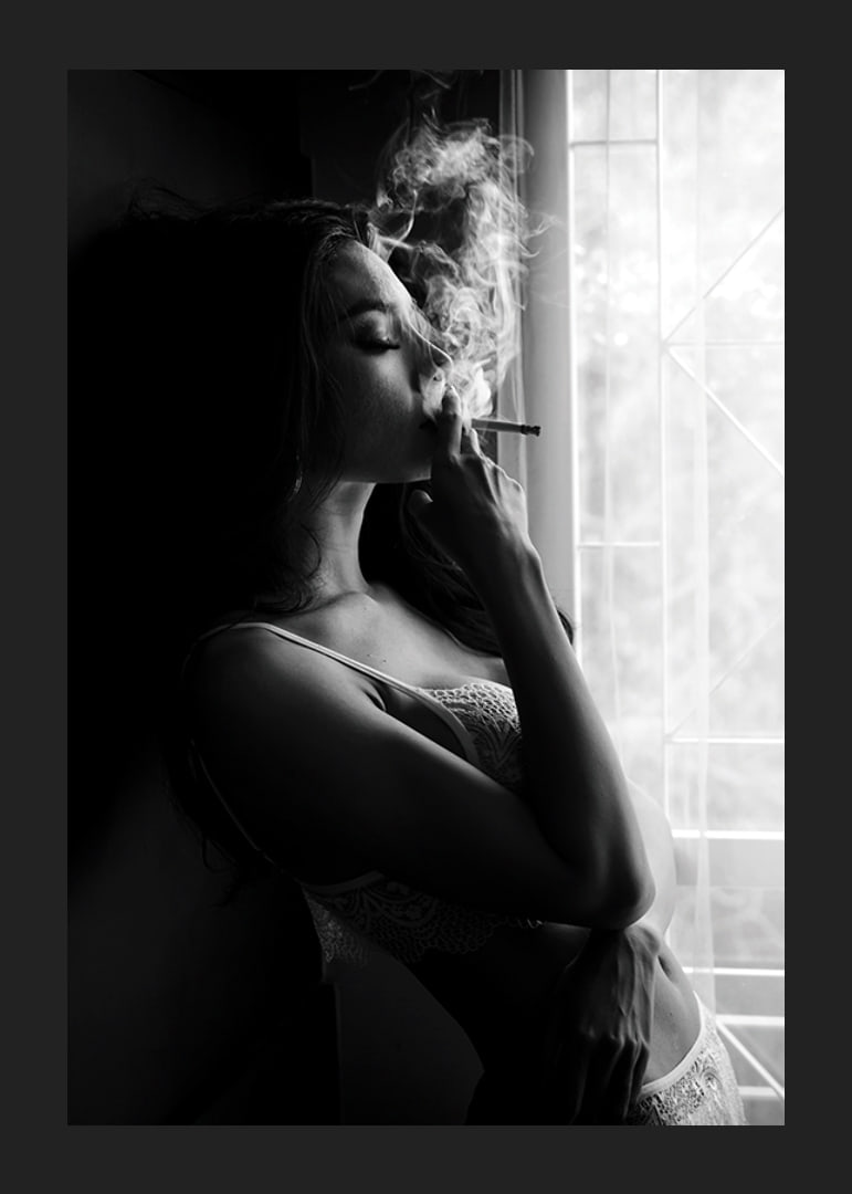 Black and white photograph of woman smoking by a window-12