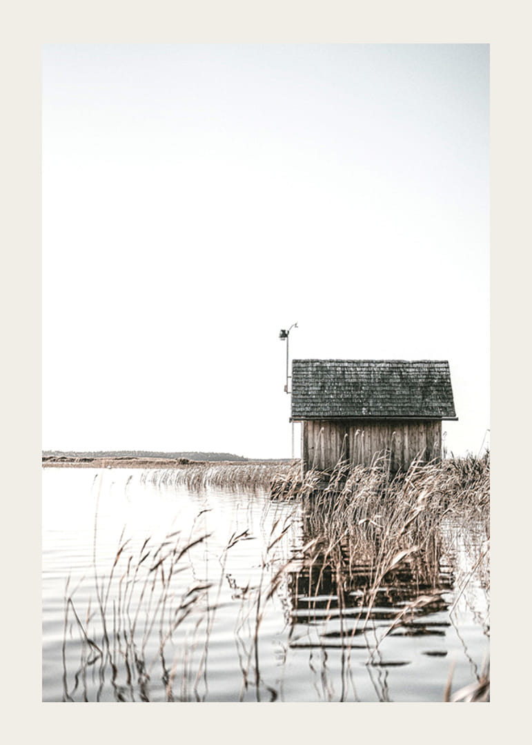 Motivo fotográfico de una cabaña de madera junto a los juncos y un lago tranquilo.-12