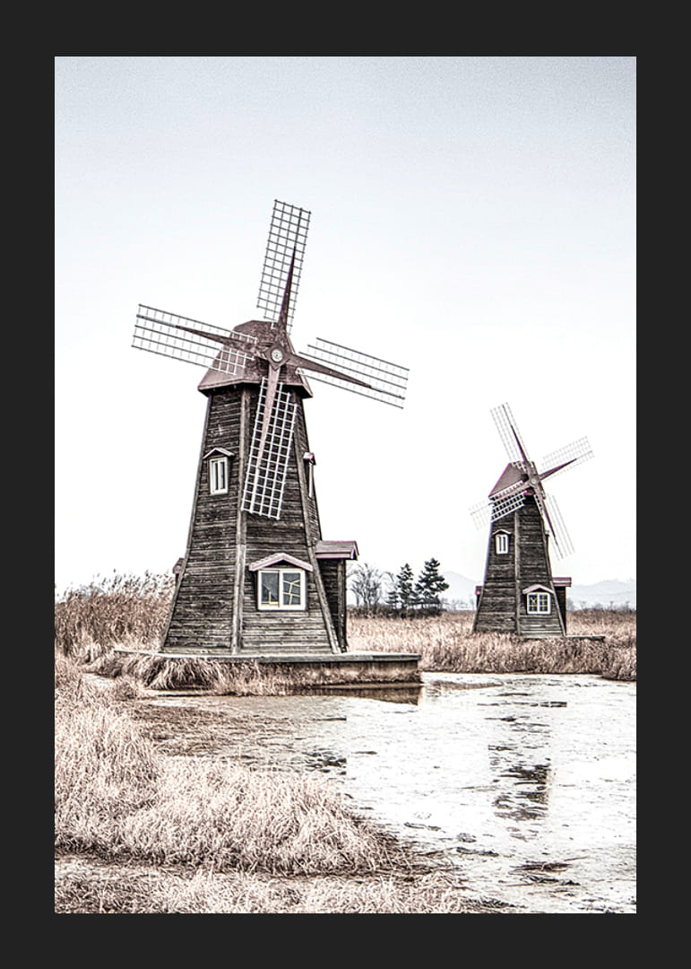 Valokuva kahdesta vanhasta puisesta tuulimyllystä ruo'on ja veden äärellä-12