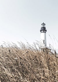 Fotografía de un faro blanco detrás de un césped alto de color beige contra un cielo brillante.-7