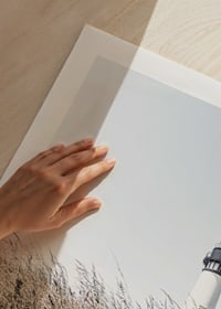 Fotografía de un faro blanco detrás de un césped alto de color beige contra un cielo brillante.-9
