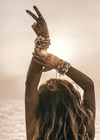 Woman with arms in the air, shell bracelet and backlight by the sea-7