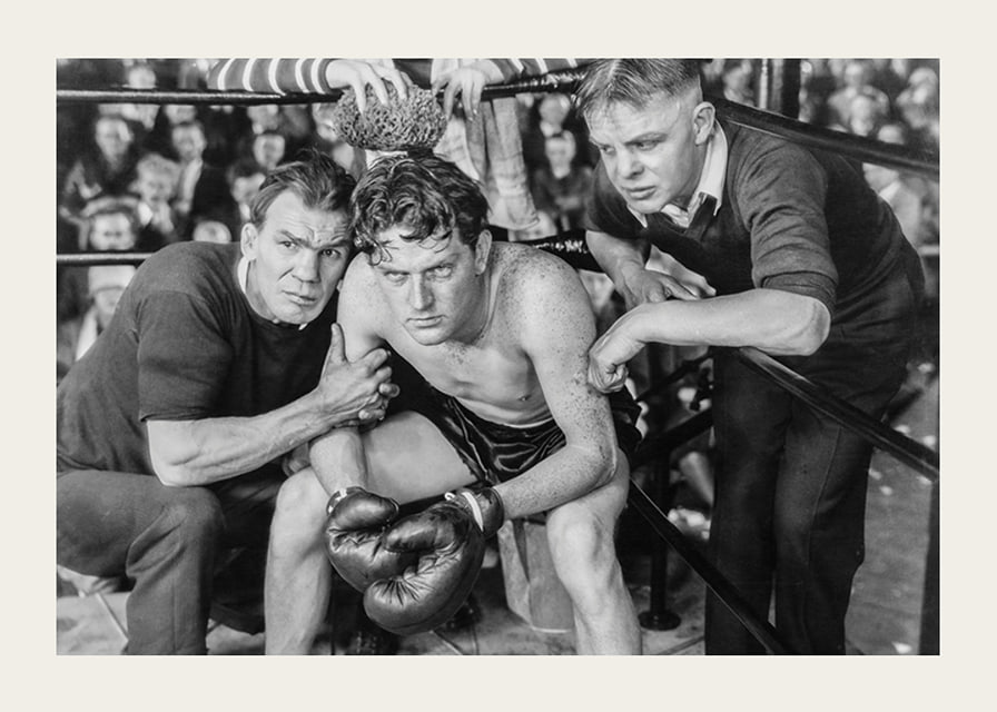 Black and white scene with boxer and two trainers in ring corner-12