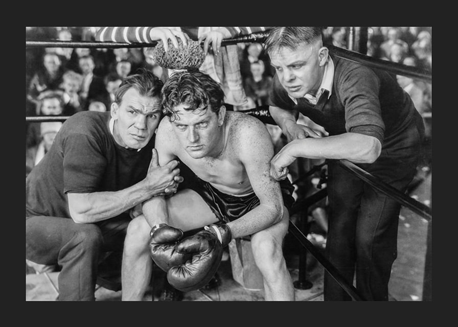 Black and white scene with boxer and two trainers in ring corner-12