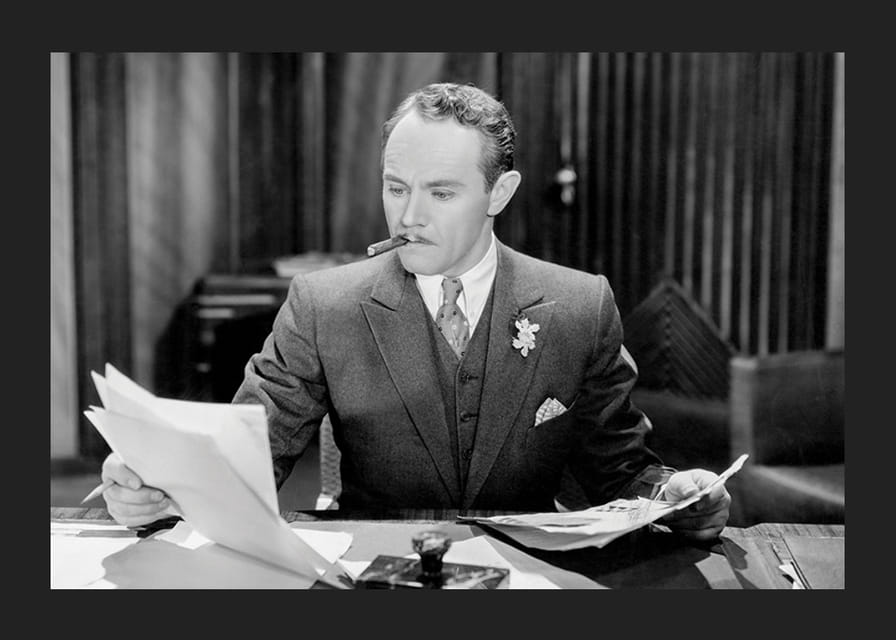 Svartvitt foto av man i kostym med cigarr vid skrivbord-12