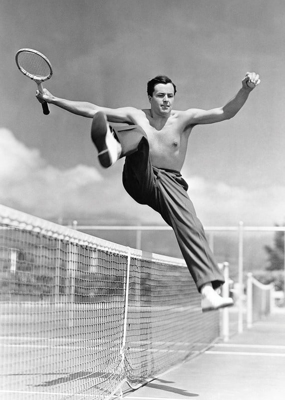 Black and white photo of bare-chested man jumping over tin netting-12