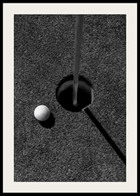 Black and white close-up of golf ball next to hole with flagpole-2