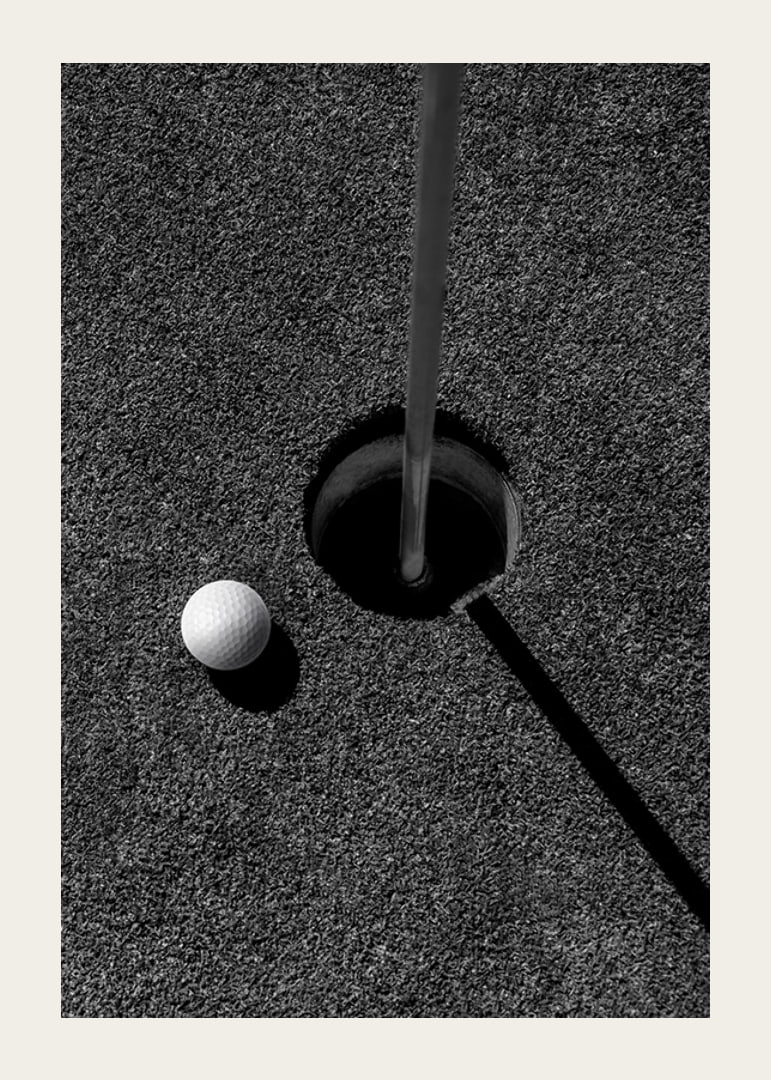 Black and white close-up of golf ball next to hole with flagpole-12