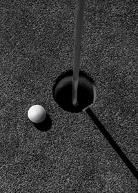 Black and white close-up of golf ball next to hole with flagpole-7