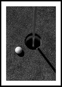 Black and white close-up of golf ball next to hole with flagpole-0