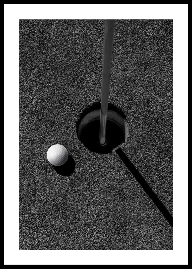 Black and white close-up of golf ball next to hole with flagpole-12
