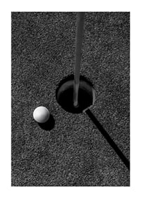 Black and white close-up of golf ball next to hole with flagpole-1