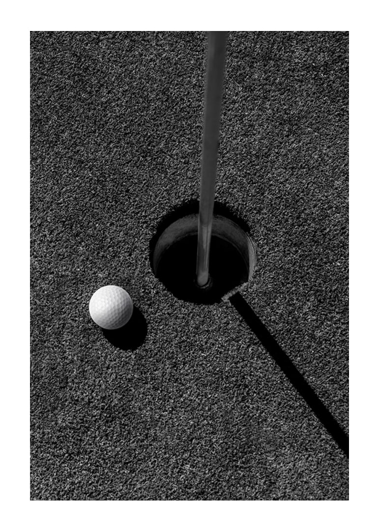 Black and white close-up of golf ball next to hole with flagpole-12