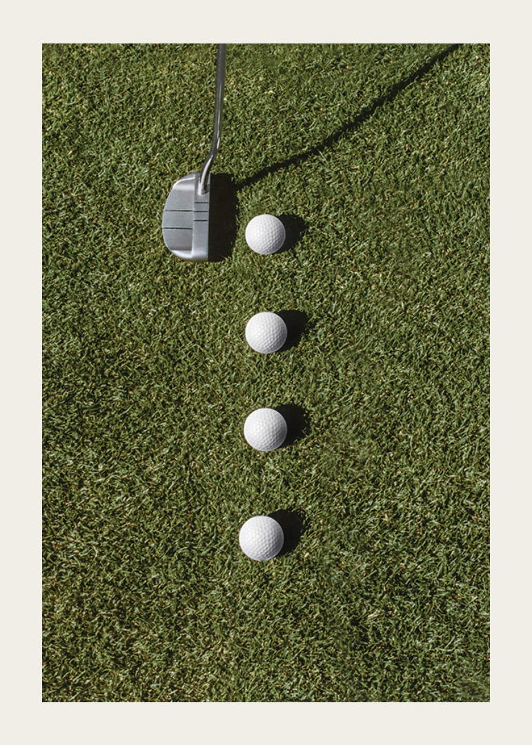 Golf club and four white golf balls on green lawn-12